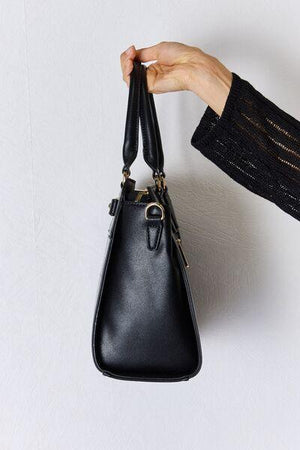 a hand holding a black purse on a white wall