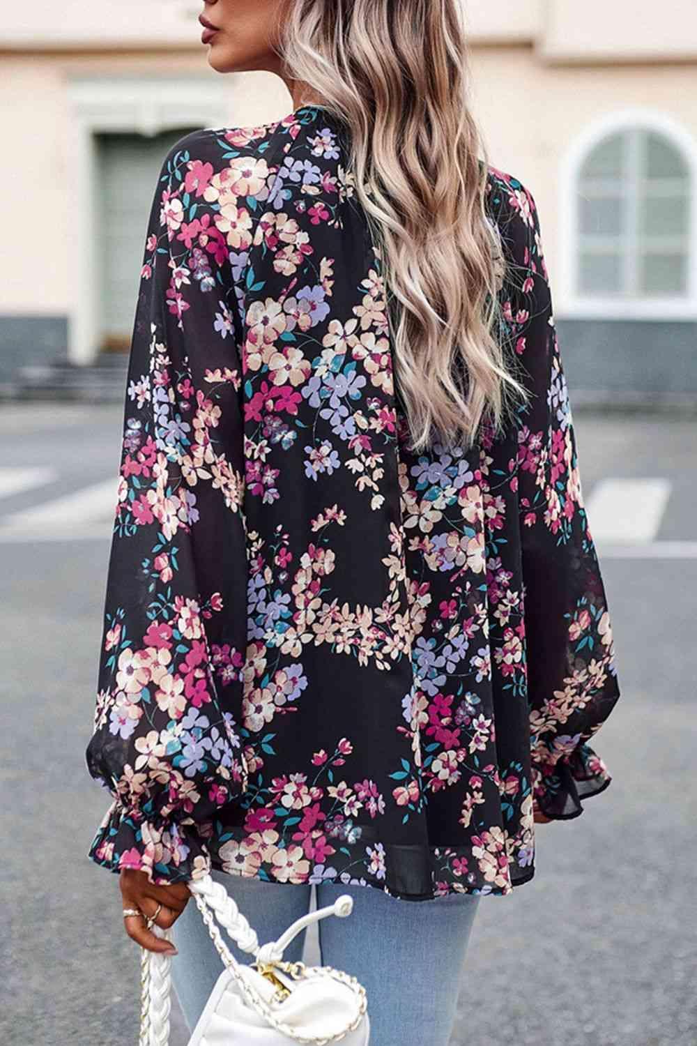 a woman wearing a black floral blouse and jeans