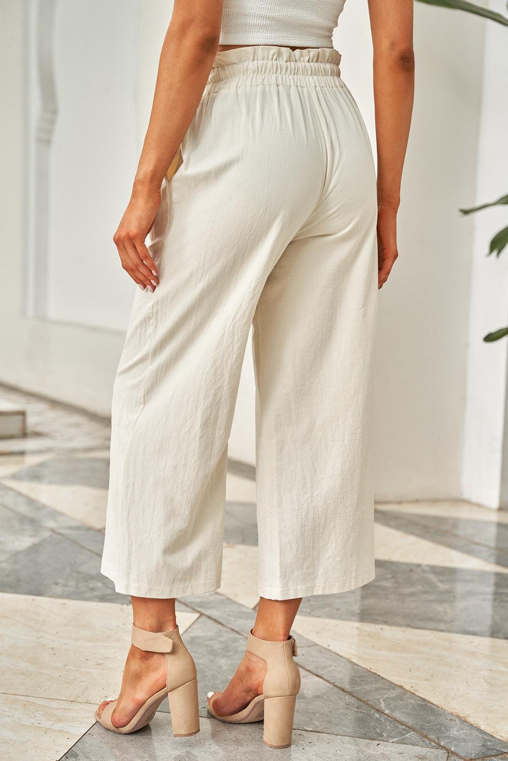 a woman standing on a tile floor wearing white pants