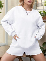 a woman sitting on a chair wearing a white sweatshirt and shorts