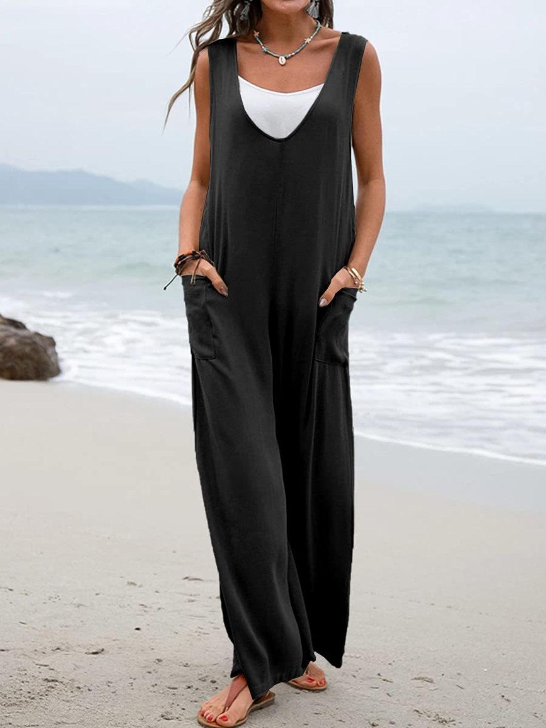 a woman standing on a beach wearing a black jumpsuit