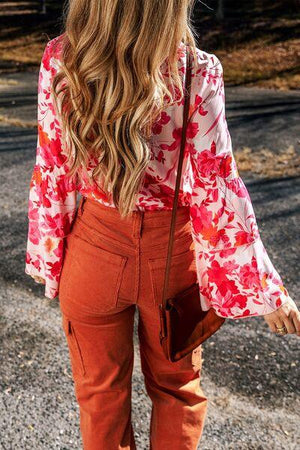 a woman with long hair wearing an orange pants and a floral blouse