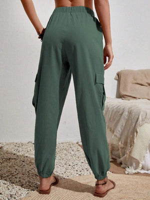 a woman standing in front of a bed wearing green pants