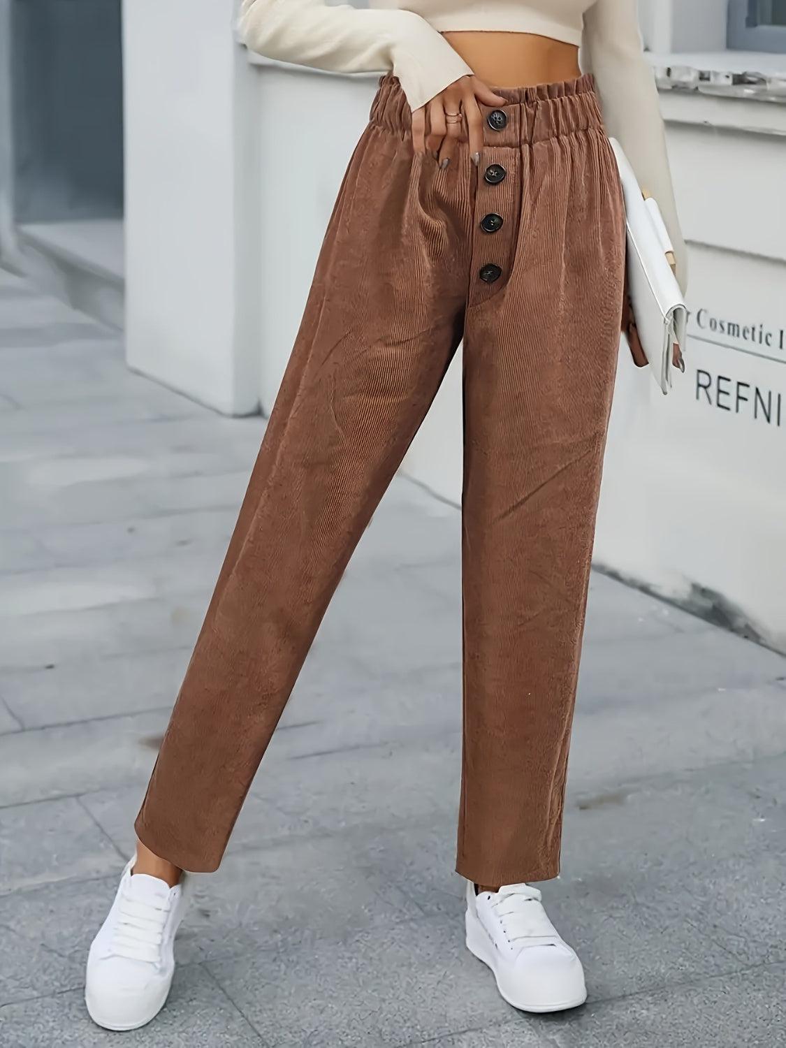 a woman standing on a sidewalk wearing brown pants