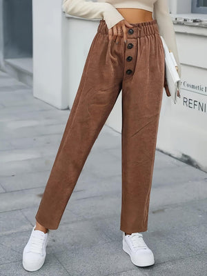 a woman standing on a sidewalk wearing brown pants