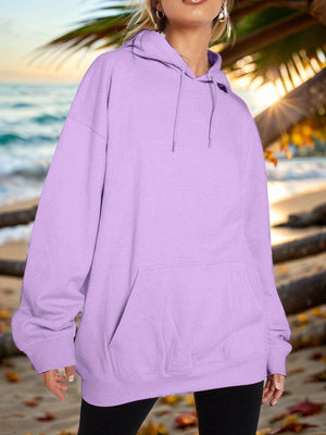 a woman standing on a beach wearing a purple hoodie