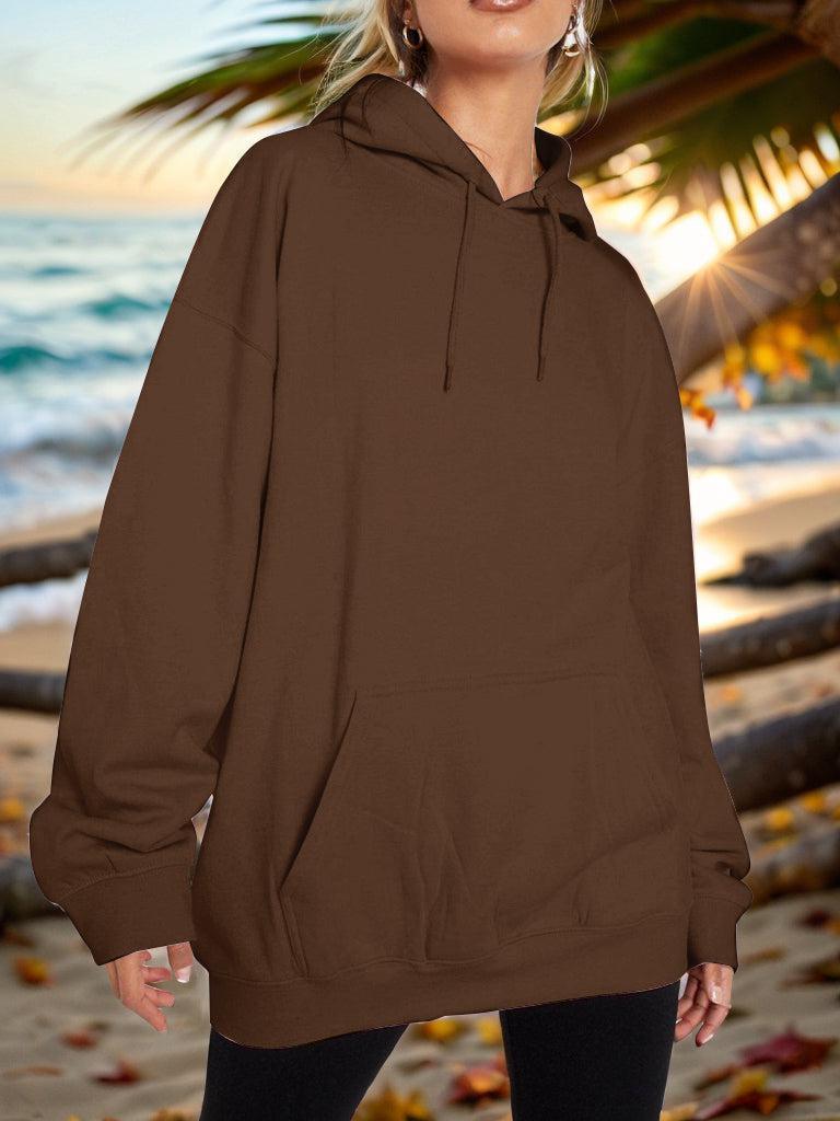 a woman standing on a beach wearing a brown hoodie