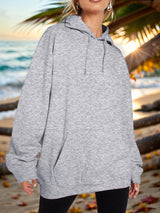 a woman standing on a beach wearing a gray hoodie