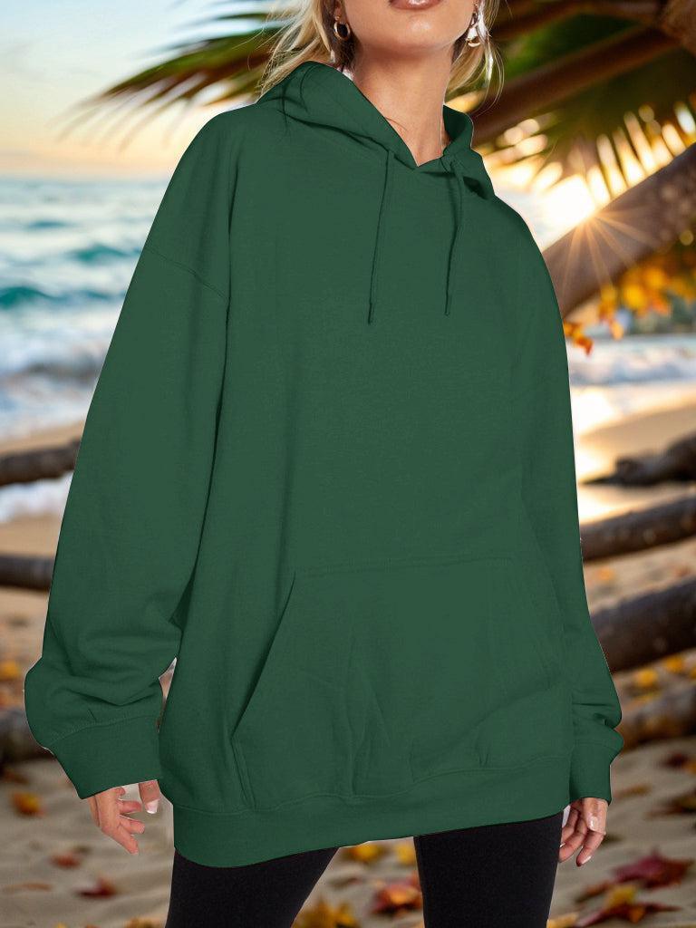 a woman standing on a beach wearing a green hoodie