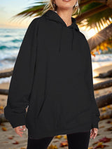 a woman standing on a beach wearing a black hoodie