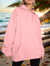 a woman standing on a beach wearing a pink hoodie