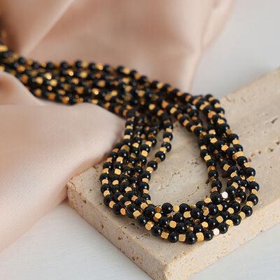 a black and gold beaded necklace sitting on top of a wooden block