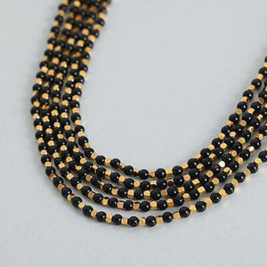 a black and gold beaded necklace on a white surface