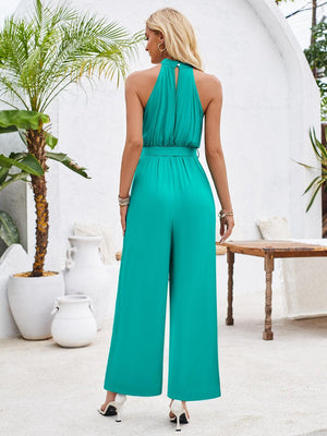 a woman in a green jumpsuit standing in front of a palm tree