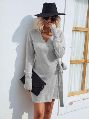 a woman leaning against a wall wearing a gray sweater dress