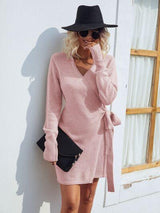 a woman leaning against a wall wearing a pink sweater dress