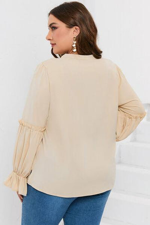 a woman wearing a beige top with ruffled sleeves