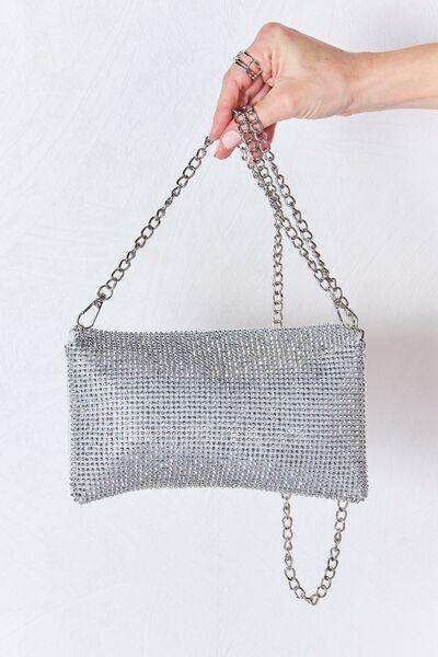 a hand holding a silver purse with chains
