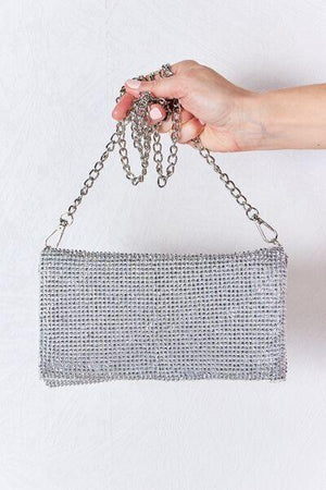 a hand holding a silver purse with a chain