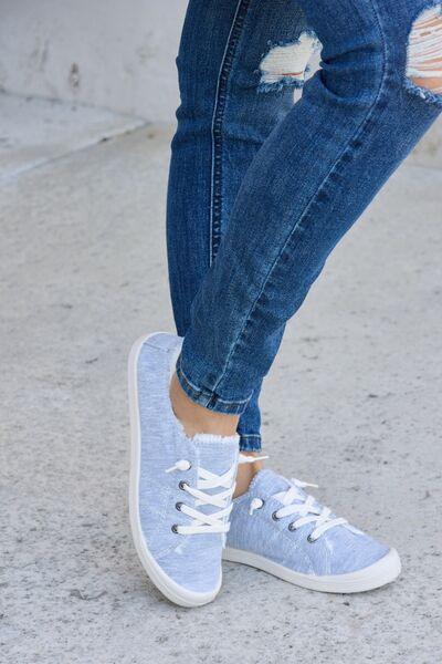 a woman in ripped jeans and blue sneakers