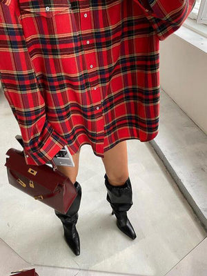 a woman in a red plaid dress holding a brown purse