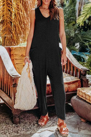 a woman in a black jumpsuit holding a white bag