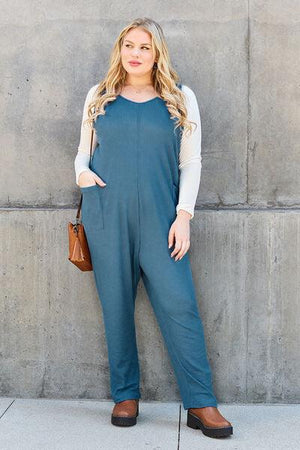 a woman standing in front of a wall wearing a blue jumpsuit