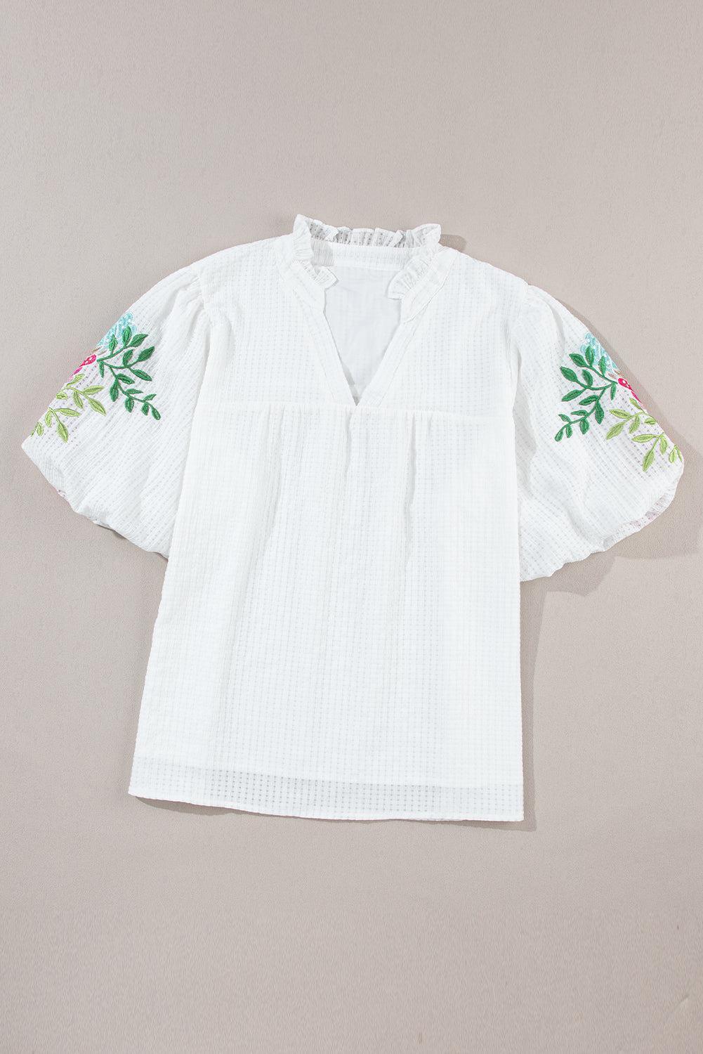 a white top with a flower embroidered on it