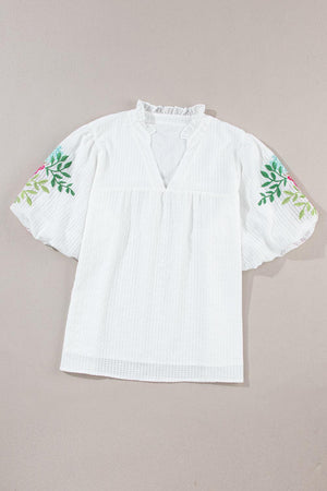 a white top with a flower embroidered on it