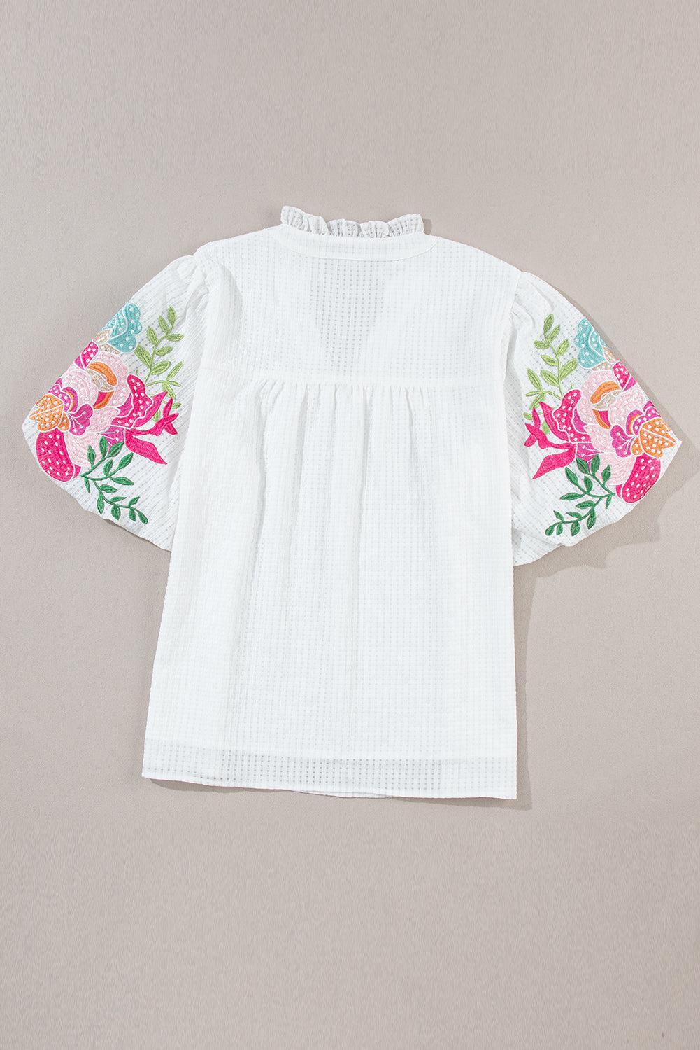 a white top with a floral design on the sleeves