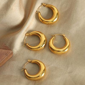 three pairs of gold hoop earrings sitting on a cloth