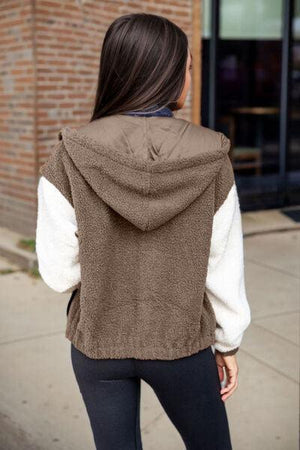 a woman standing on a sidewalk wearing a brown and white jacket