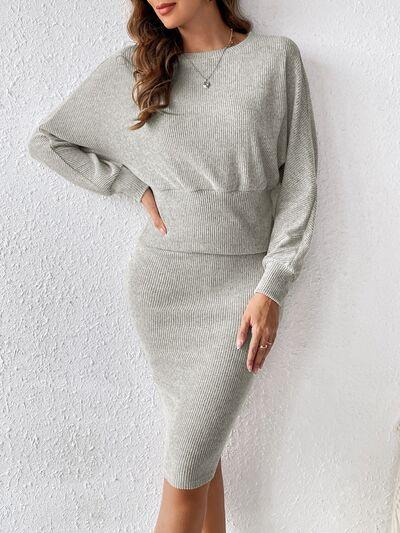 a woman in a grey sweater dress leaning against a wall