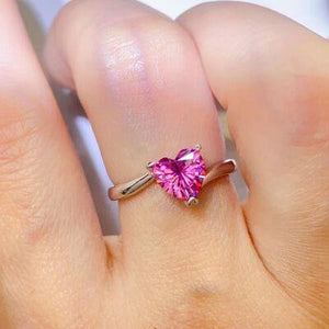 a woman's hand holding a pink heart shaped ring