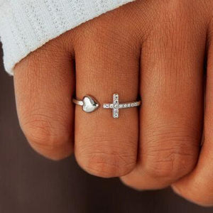 a close up of a person's hand with a cross and heart ring