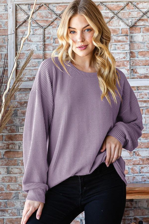 a woman standing in front of a brick wall wearing a purple sweater
