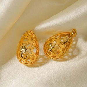 a pair of gold earrings sitting on top of a white cloth