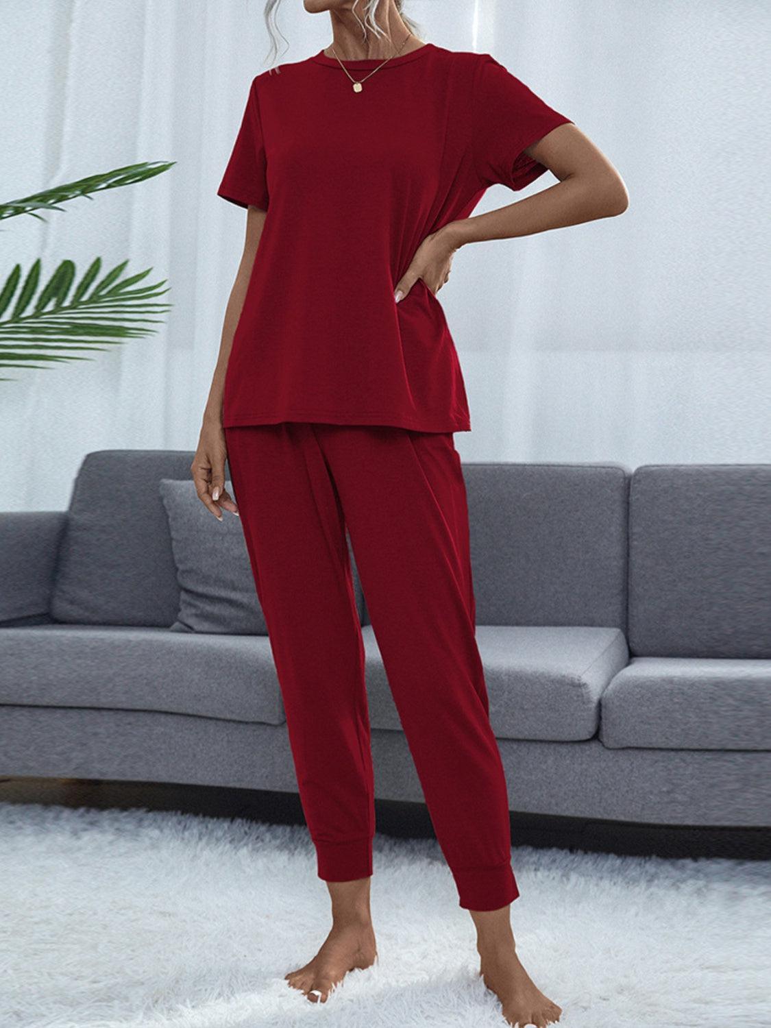 a woman standing in a living room wearing a red top and pants