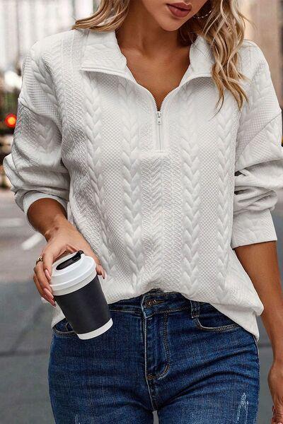 a woman holding a coffee cup and wearing a white sweater