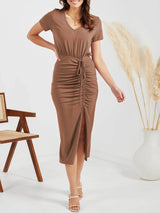 a woman standing in front of a chair wearing a brown dress