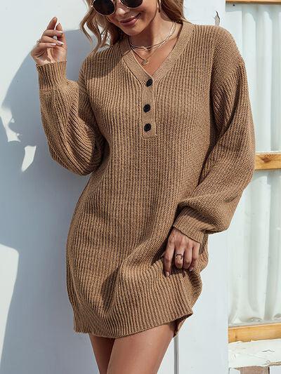 a woman in a brown sweater dress leaning against a wall