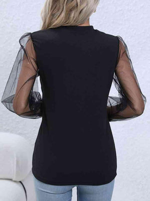 a woman wearing a black top with sheer sleeves