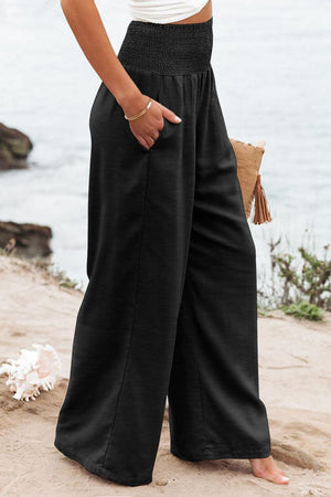 a woman standing on a beach wearing a white top and black pants