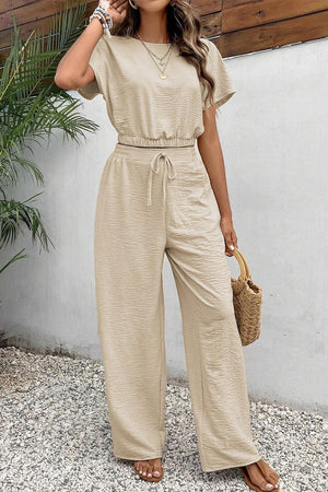 a woman wearing a tan jumpsuit and a straw bag