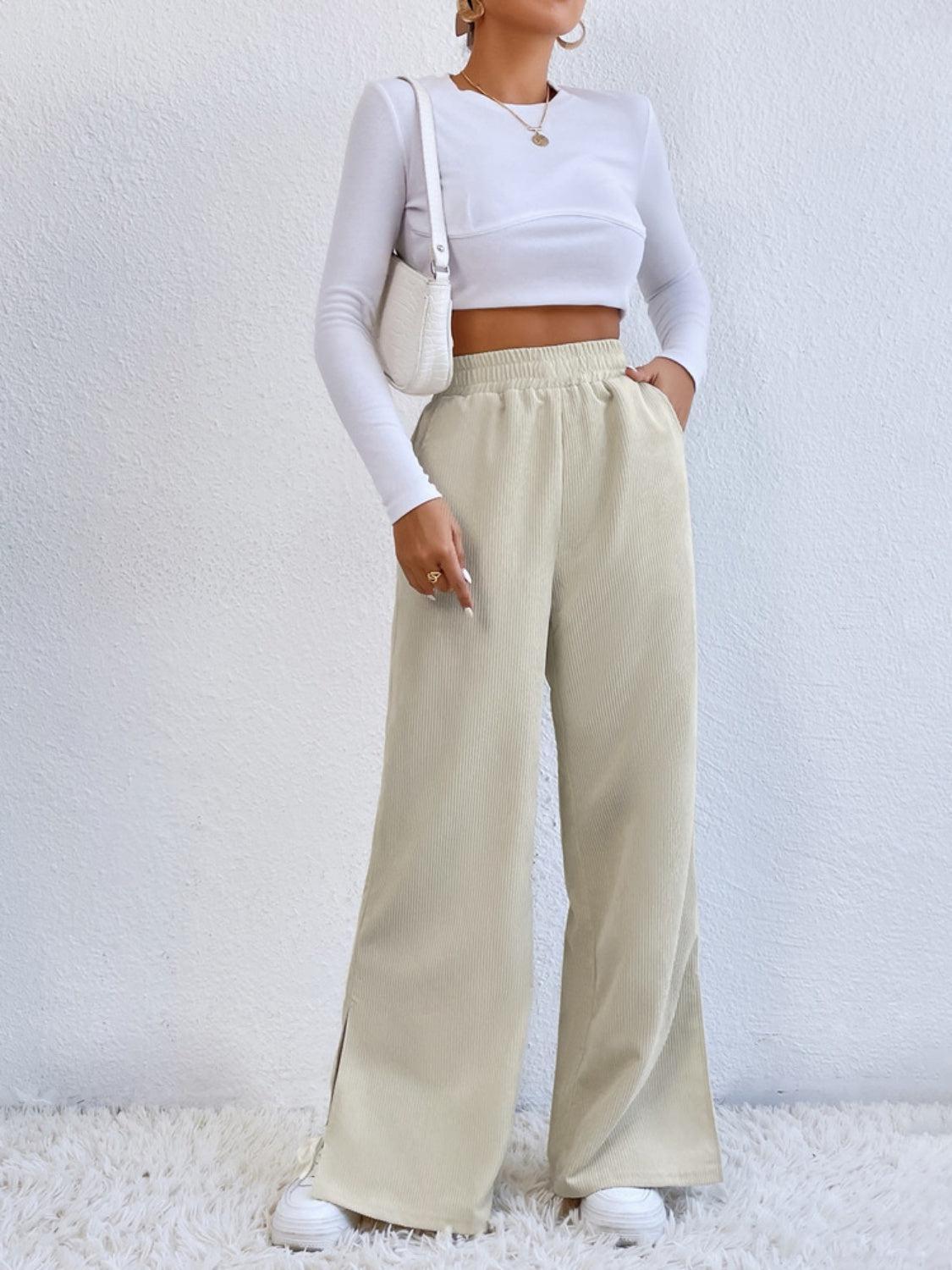 a woman wearing a white crop top and beige wide legged pants