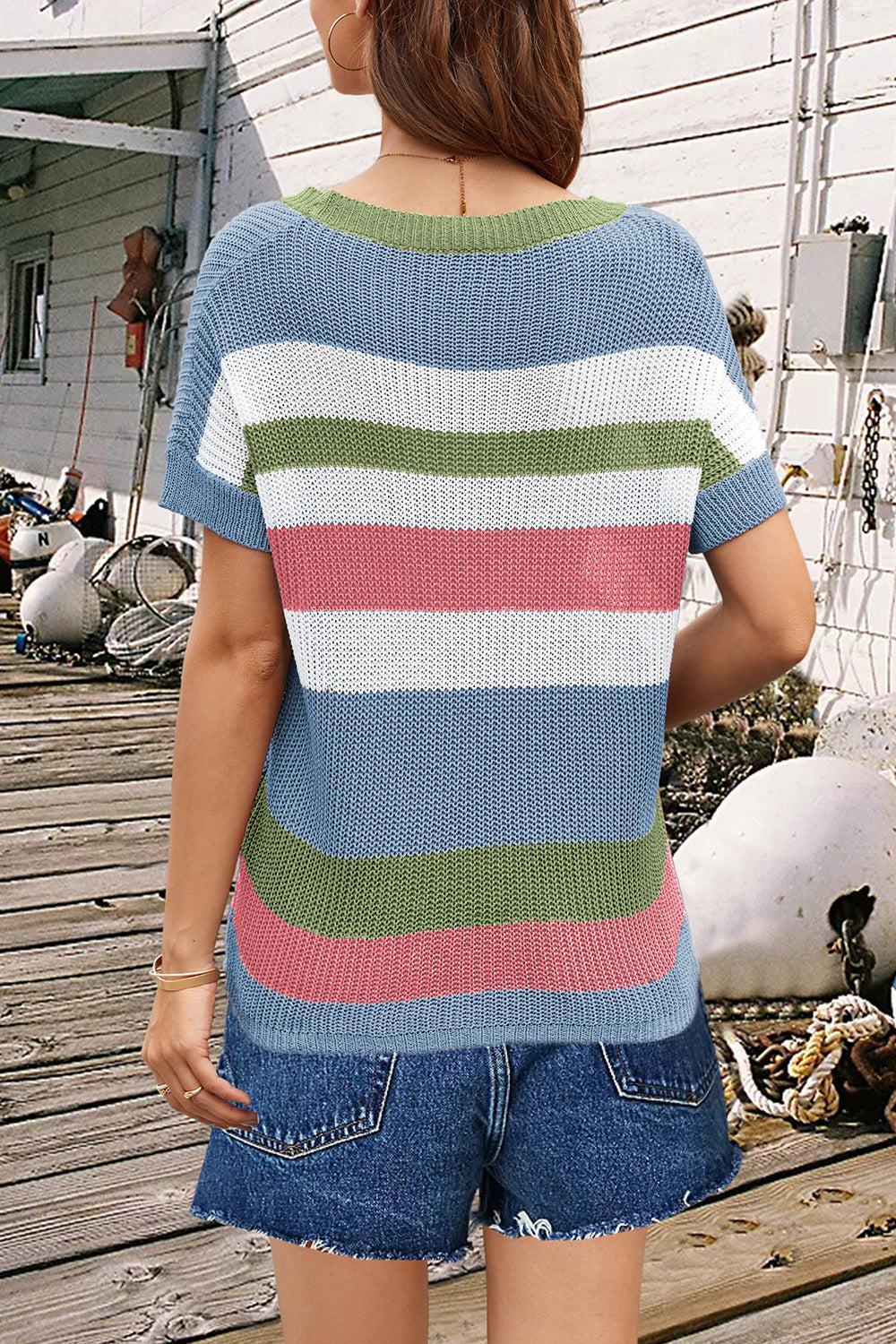 a woman standing on a wooden deck wearing a multicolored sweater