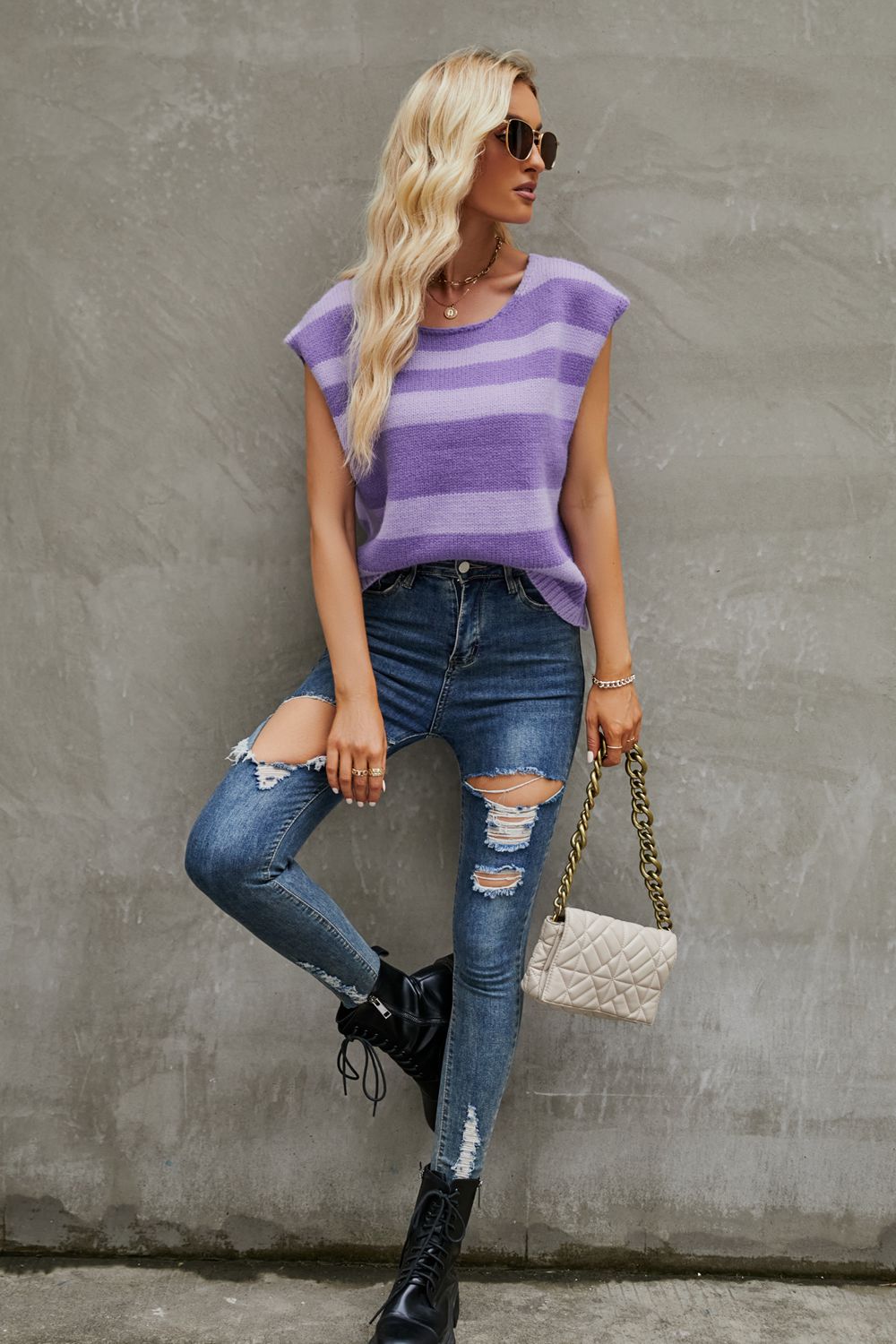 a woman leaning against a wall wearing ripped jeans