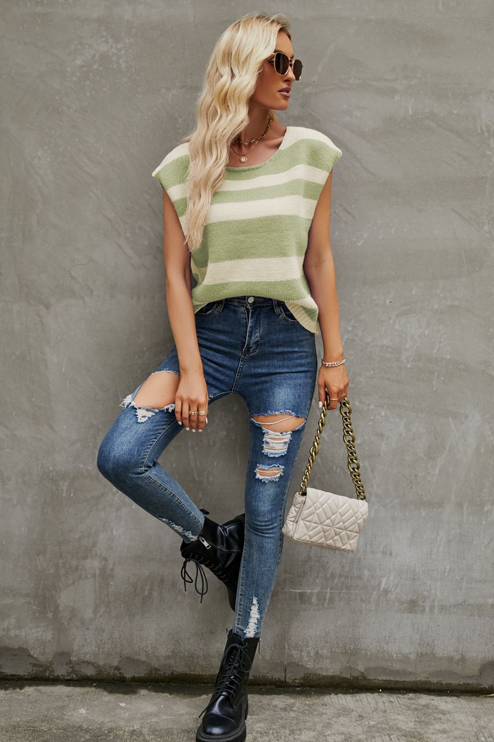 a woman leaning against a wall wearing ripped jeans