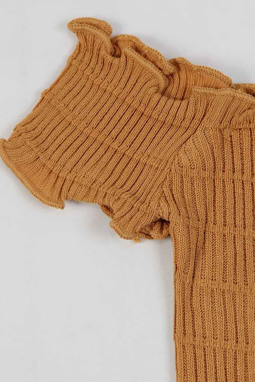 a brown sweater with ruffles is laying on a white surface