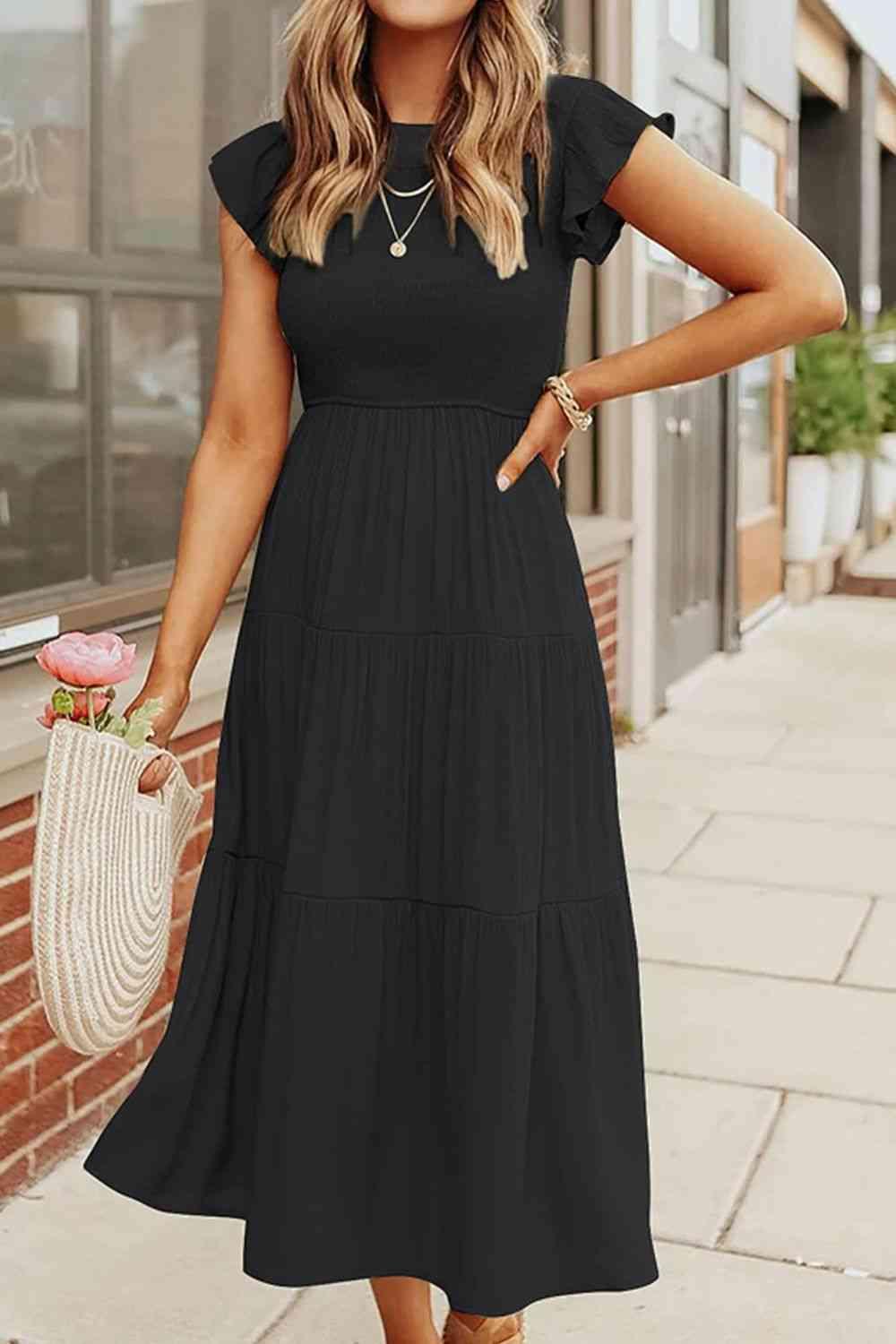 a woman in a black dress standing on a sidewalk